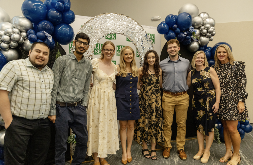 a group of people stand posed and smiling in front of a decorative ballon and arch backdrop