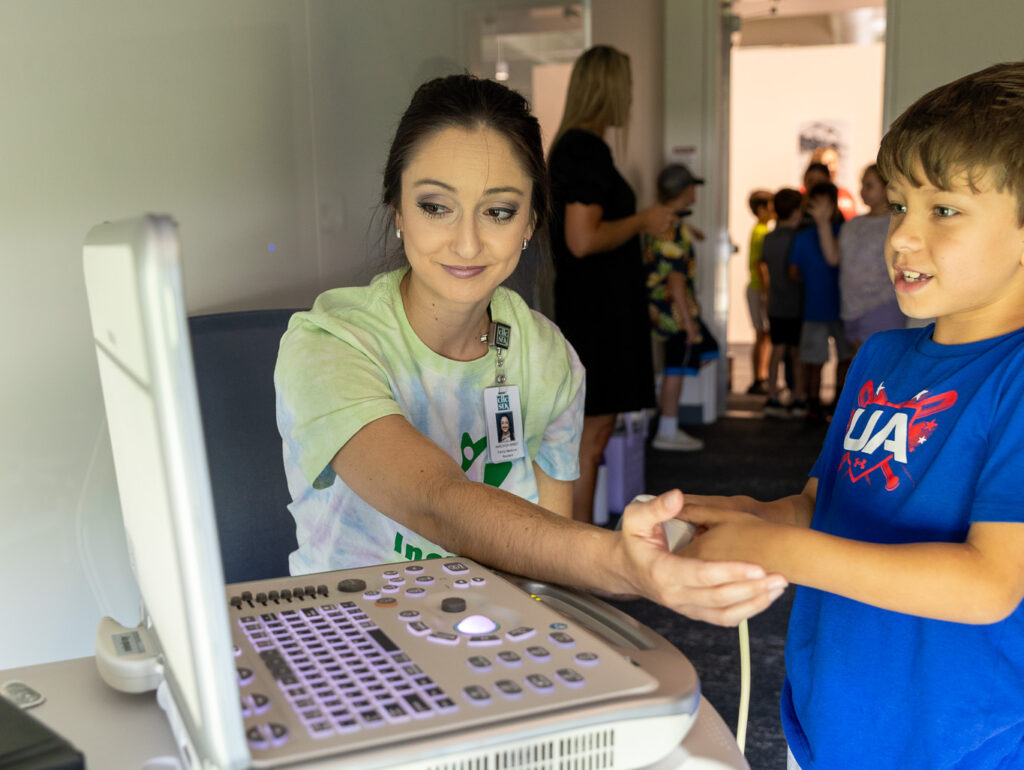 family medicine resident demonstrates to child how to use ultrasound machine on arm